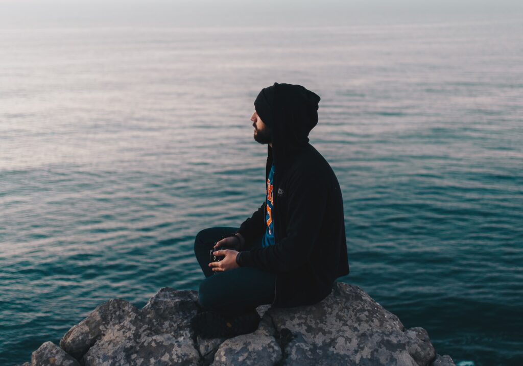 man sitting on rock near ocean water